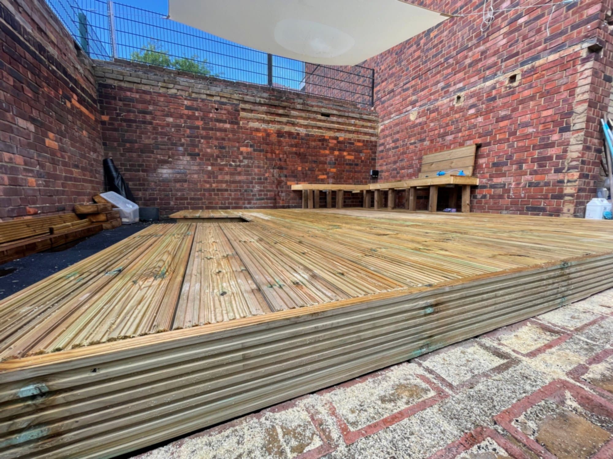 A finished hardwood deck filling the whole of a Stratford back garden, with a built-in raised bench along the back wall and corrugated metal edging
